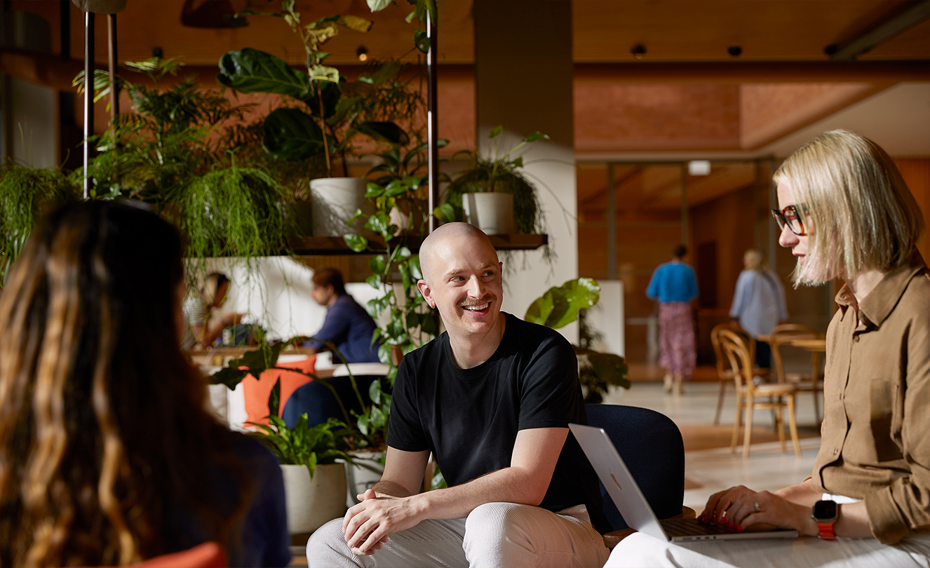 ثلاثة موظفين من فريق Apple يجلسون معاً وأحدهم يحمل جهاز MacBook، بينما يتحدثون أثناء الجلوس على كراسي بذراعين في Caffè Macs.